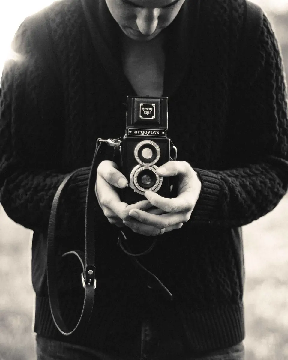 Basalto segura uma câmara antiga junto ao peito, fotografia a preto e branco.